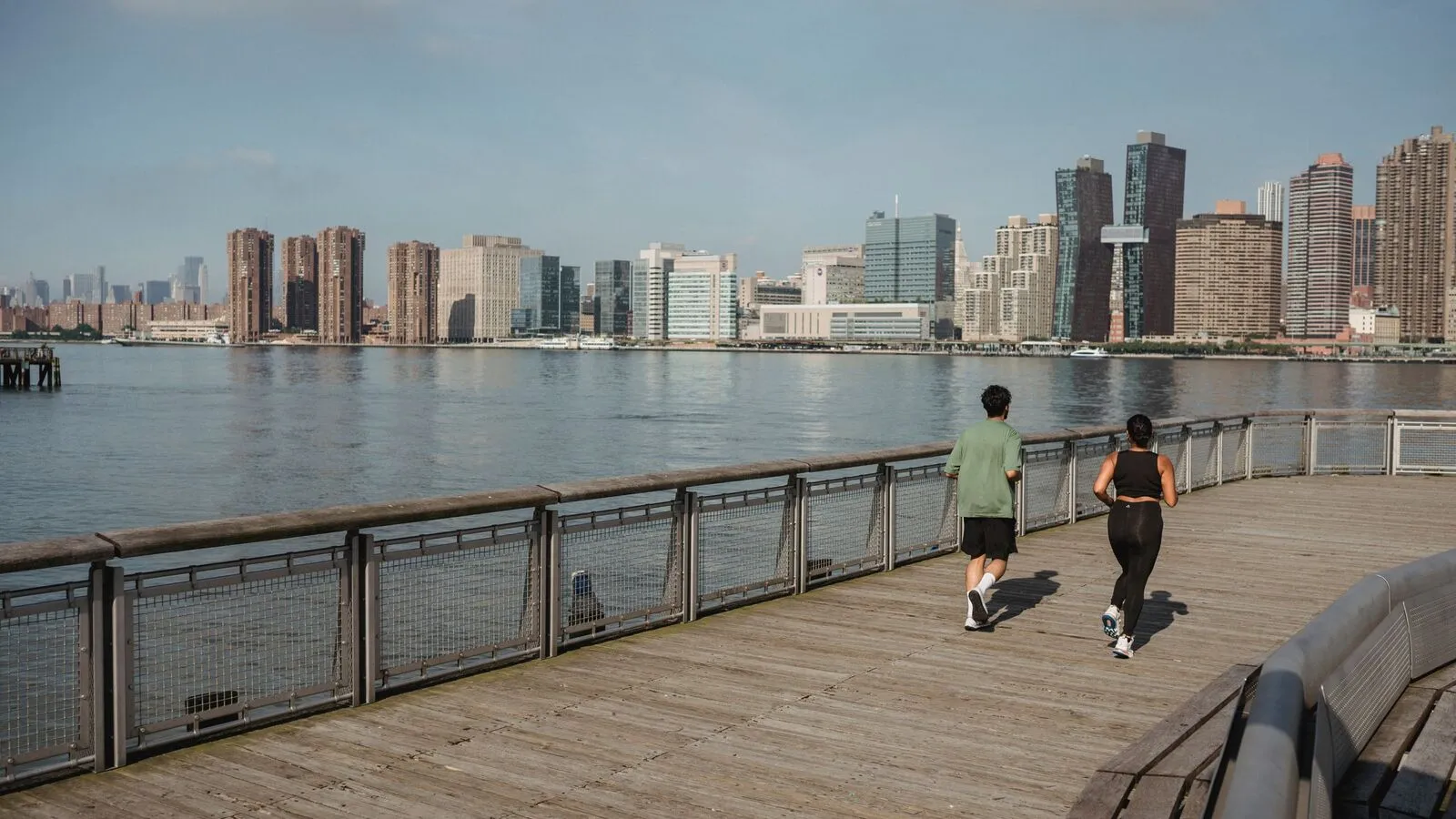Dos personas corriendo junto al río con la ciudad al fondo (foto de ejemplo)